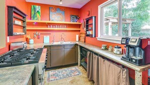 Una cocina con estufa a gas, lavaplatos y cafetera. Hay estantes con vajilla y una ventana con vistas a la vegetación.