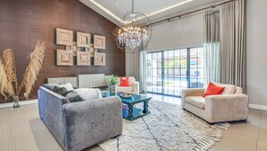 Uma sala de estar moderna com um sofá cinza, uma poltrona bege, uma mesa de centro e um candelabro.