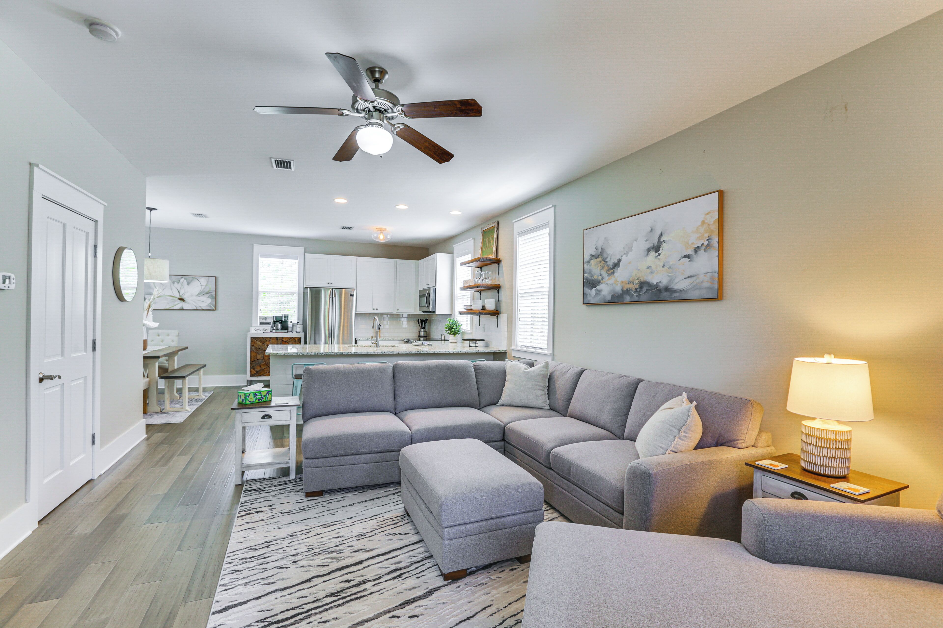 A modern living room with a grey sectional sofa, a white rug, and a ceiling fan.