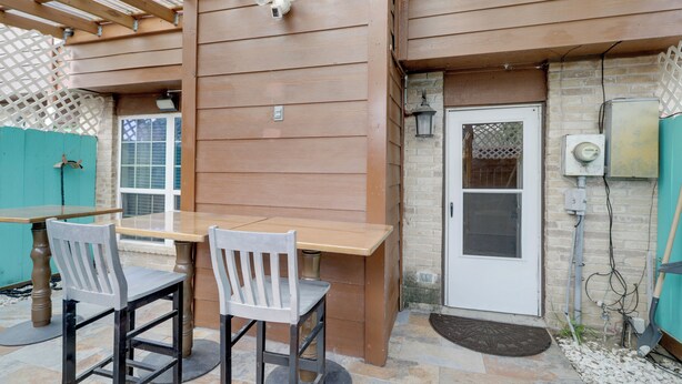 Un espace extérieur aménagé en patio, avec une table en bois et deux chaises, une porte et un petit muret en briques.