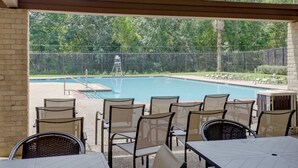Un espace extérieur avec une piscine, des chaises et des tables, le tout entouré d’une clôture et d’arbres.
