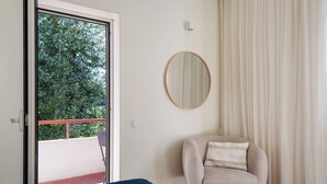 A bedroom with a bed, a chair, a round mirror, and a balcony with a red railing. - Acm021 Bombarda Homes, Spacious 3BR for Families (Porto)