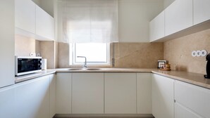 A modern kitchen with white cabinets, a built-in microwave, a sink, and a window with a white blind. - Acm021 Bombarda Homes, Spacious 3BR for Families (Porto)