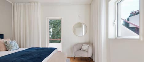 A bedroom with a bed, a chair, a round mirror, and a window.