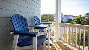 A porch with two Adirondack chairs and a small table, overlooking a residential area with houses and greenery.