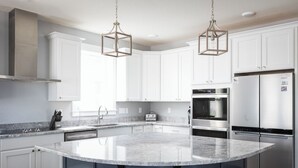 A modern kitchen with white cabinets, a large island with bar stools, stainless steel appliances, and pendant lighting.