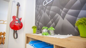 A room with a red guitar hanging on the wall, a wooden shelf with blue folders, and decorative items including green plants and a white lace doily.