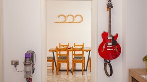 A dining area with a wooden table and chairs, a red electric guitar mounted on the wall, and a vacuum cleaner on the floor.