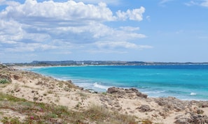 A coastal landscape with clear skies, sandy terrain, and a view of the sea.