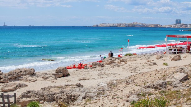 A beach with a rocky shoreline, a lifeguard station, and a distant cityscape.