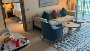 Ett hotellrum med en soffa, ett soffbord, en lekhörna för barn, ett stort fönster med utsikt över havet och en tavla på väggen.