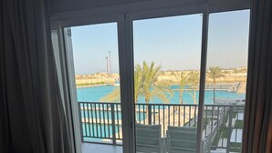 Ett hotellrum med en säng, utsikt över en pool och en balkong med stolar.