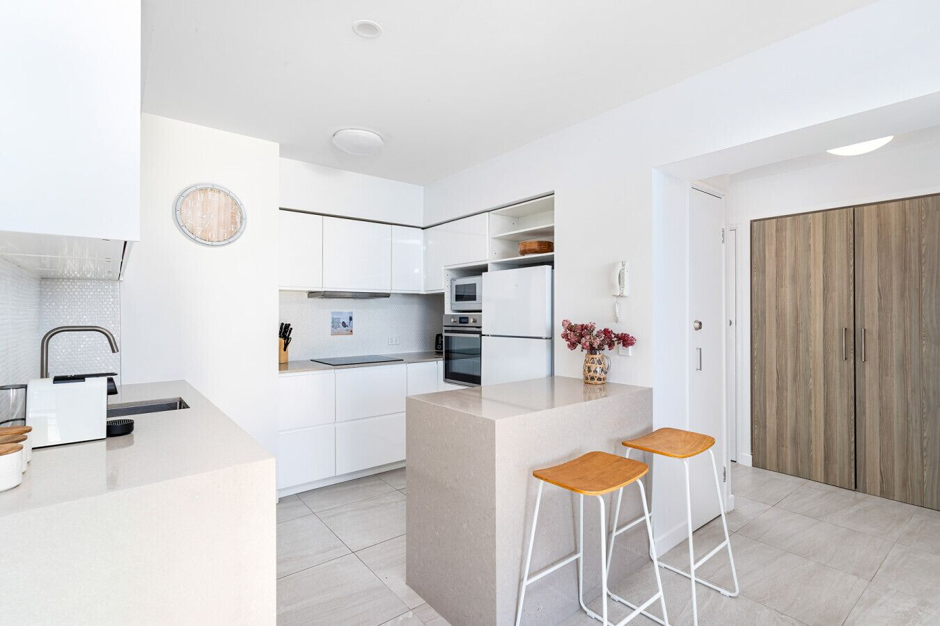 A modern kitchen with white cabinetry, a built-in oven, and a wooden door.