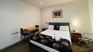 A hotel room with a bed, a desk, a chair, a bedside table, a lamp, and a painting on the wall. - Unwind Adelaide City Studio No 438 (Adelaide)