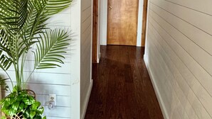 A hallway with white paneling, a wooden door at the end, and a potted plant on the left.