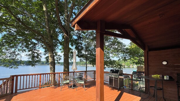 A wooden deck with a grill and outdoor seating, overlooking a lake.