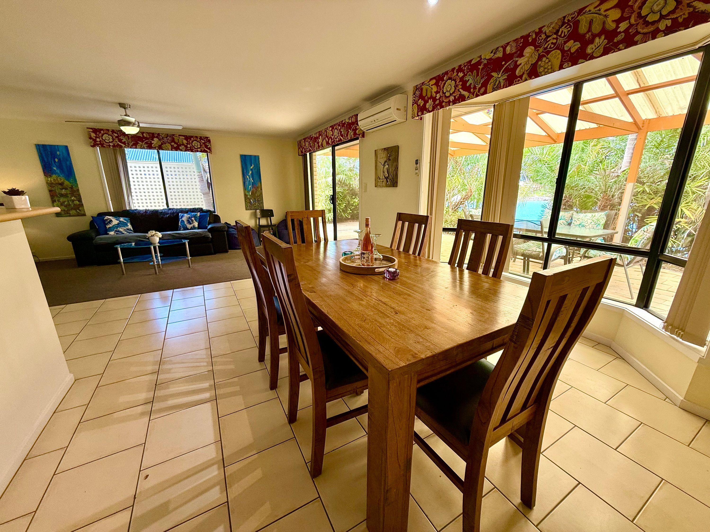 Un comedor con una mesa y sillas de madera, un sofá y ventanas amplias con cortinas.
