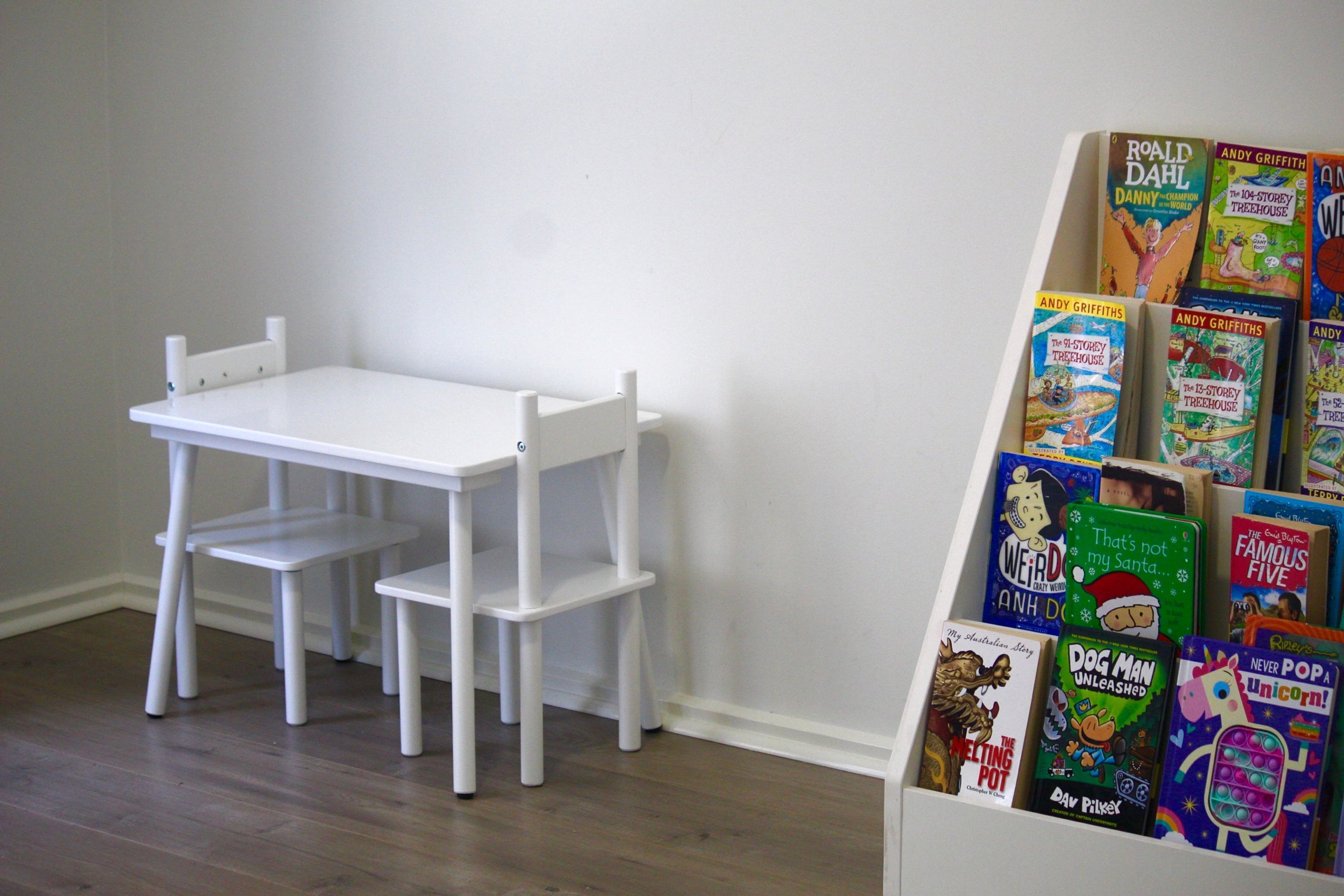 A white table and chairs in a room with a white wall and wooden flooring.