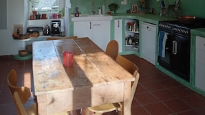 A kitchen with a wooden table, chairs, a sink, a stove, and hanging light fixtures.