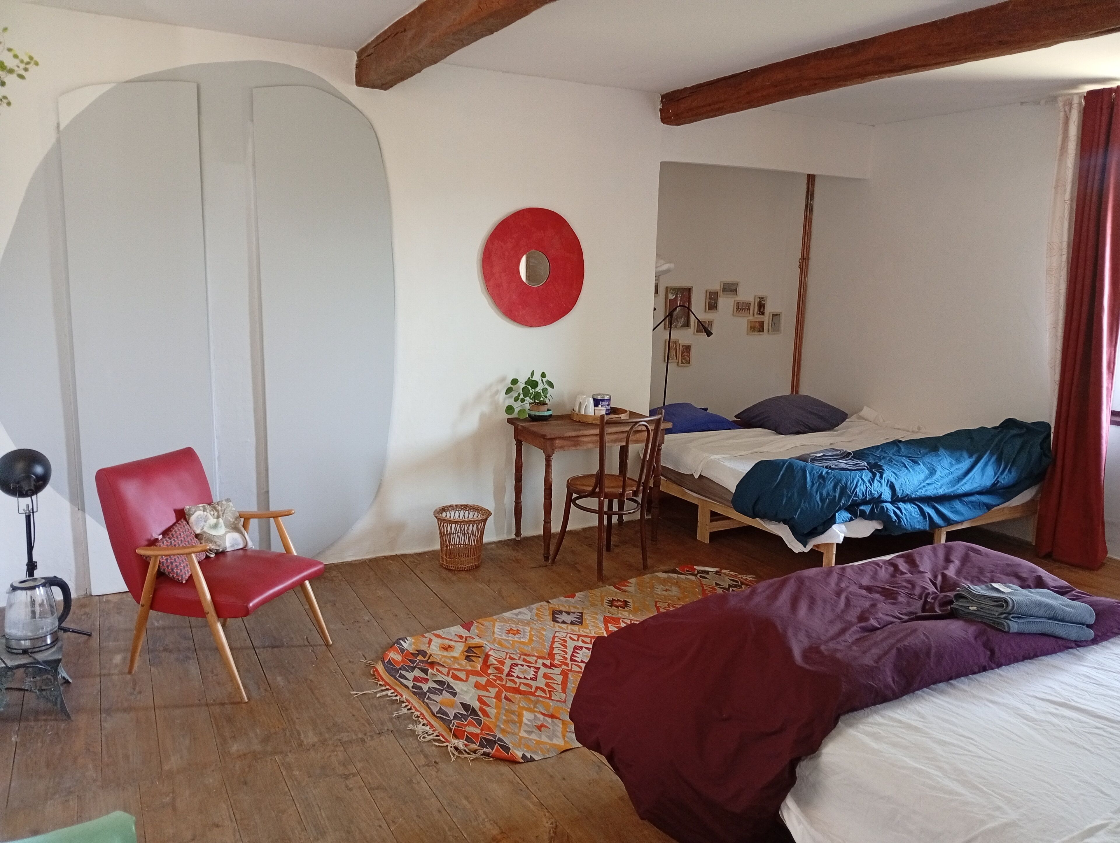 Una habitación acogedora con una cama, una silla, un escritorio y un adorno rojo en la pared.