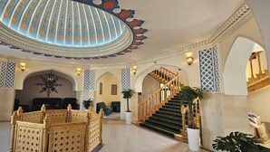 A grand lobby with a high ceiling, a staircase, and ornate wall designs.