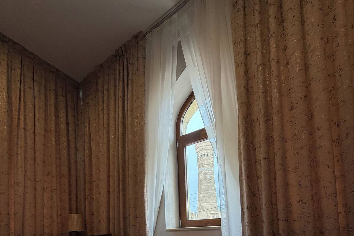 Una habitació amb un terra de fusta, un escriptori amb una cadira, un radiador i una finestra amb cortines.