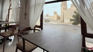 A dining area with a table and chairs, a view of a building with a tower, and a window with sheer curtains.