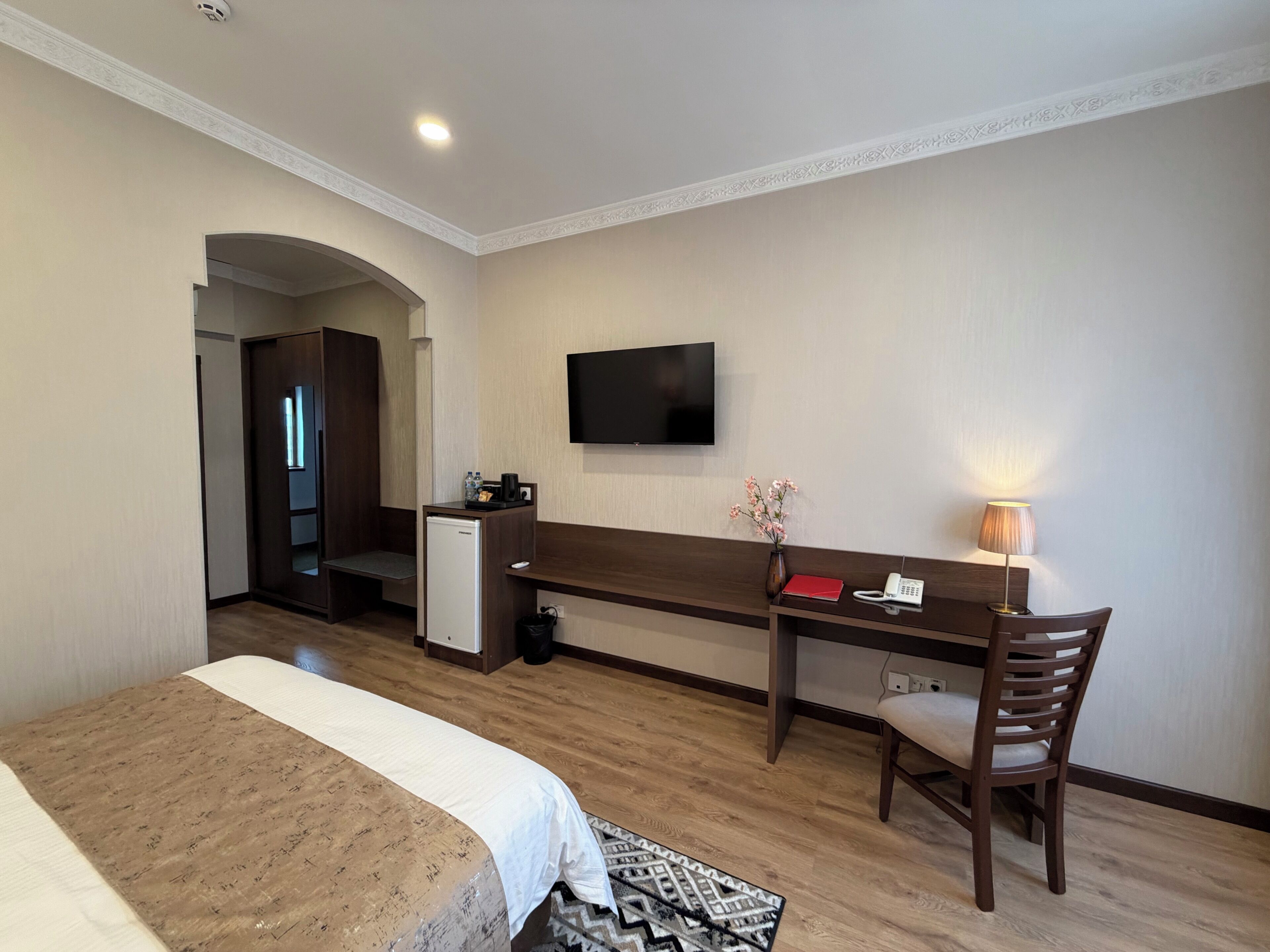 A hotel room with a bed, a desk, a chair, a TV, and a small fridge.