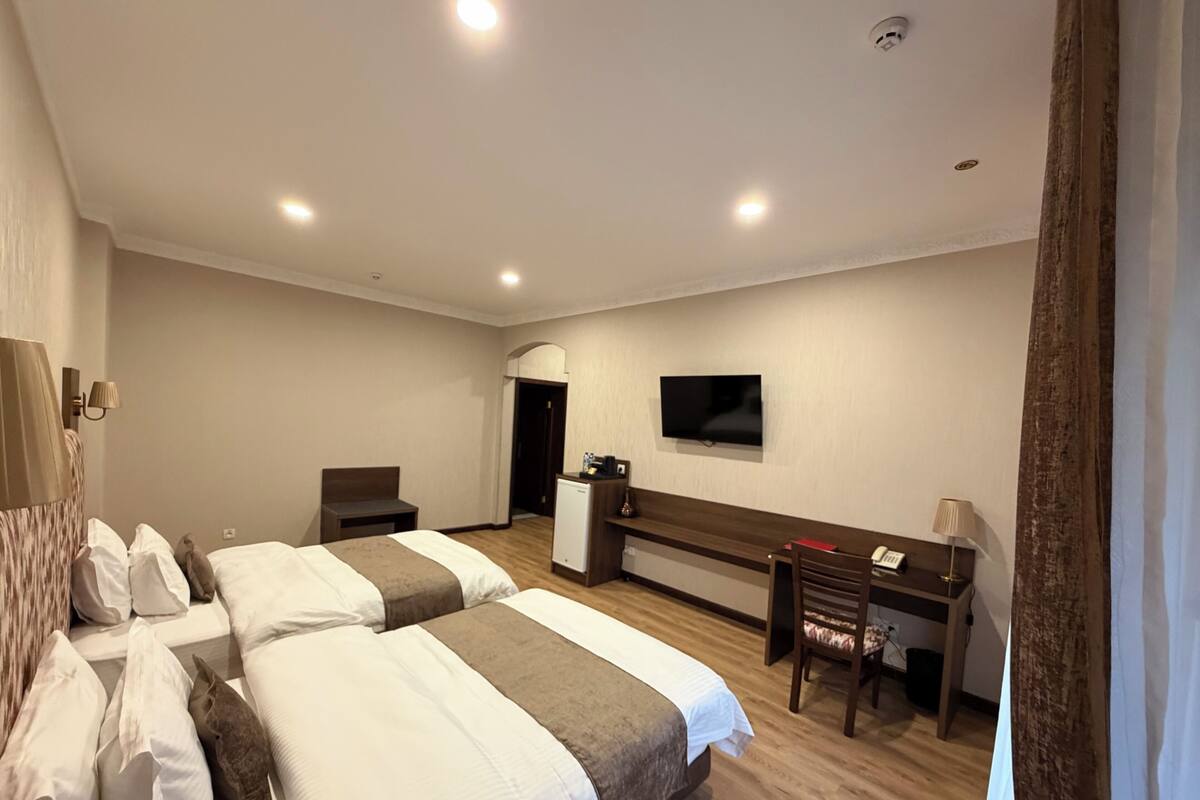 Habitació d'hotel amb dos llits, un escriptori, televisió i una cuineta petita.