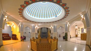A grand lobby with a central staircase, ornate ceiling, and seating area.