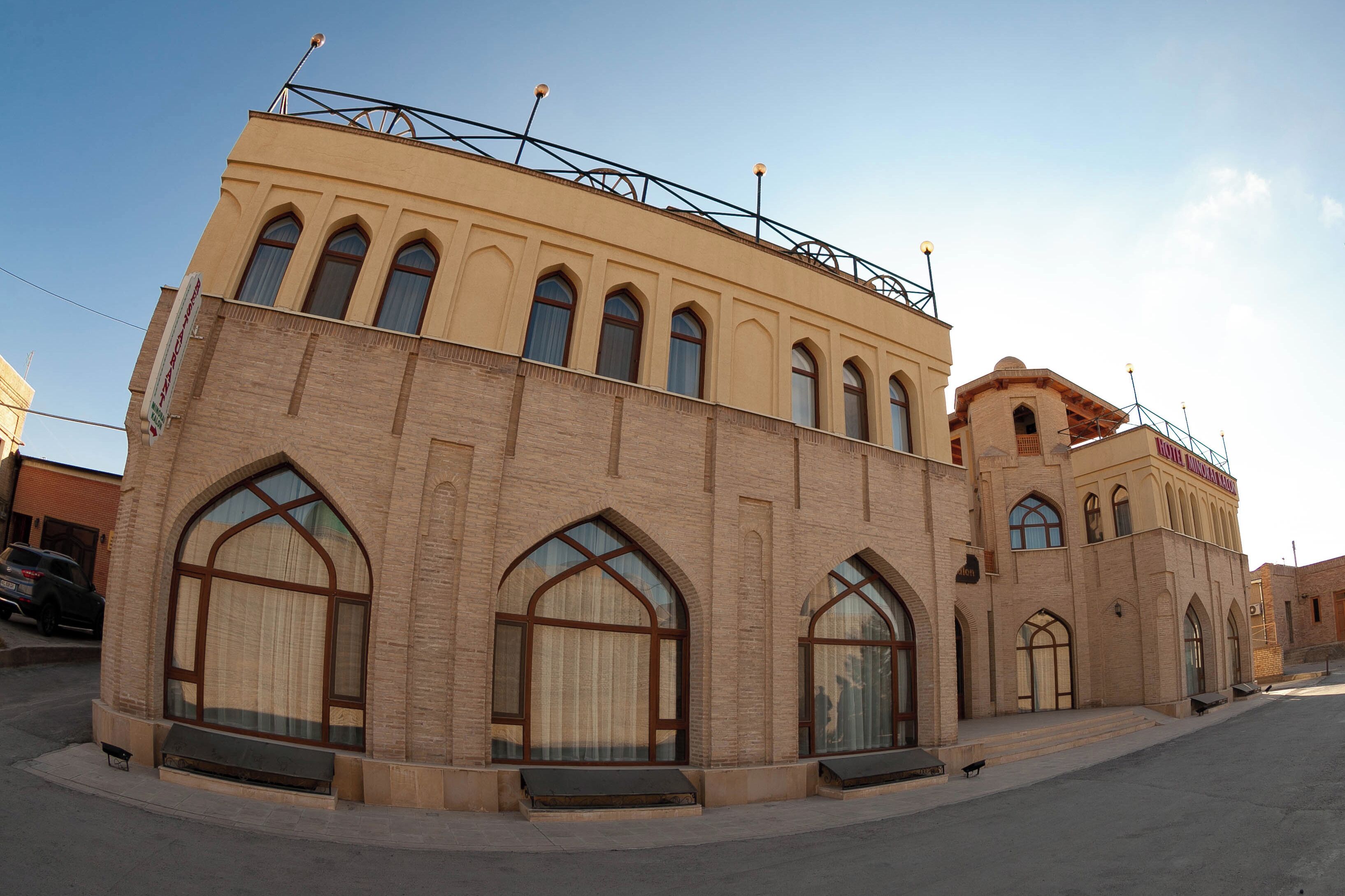 A building with arched windows and a flat roof, featuring a sign that reads "Hotel".