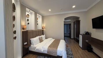 A modern hotel room with a large bed, bedside tables, a flat-screen TV, and a mirror.
