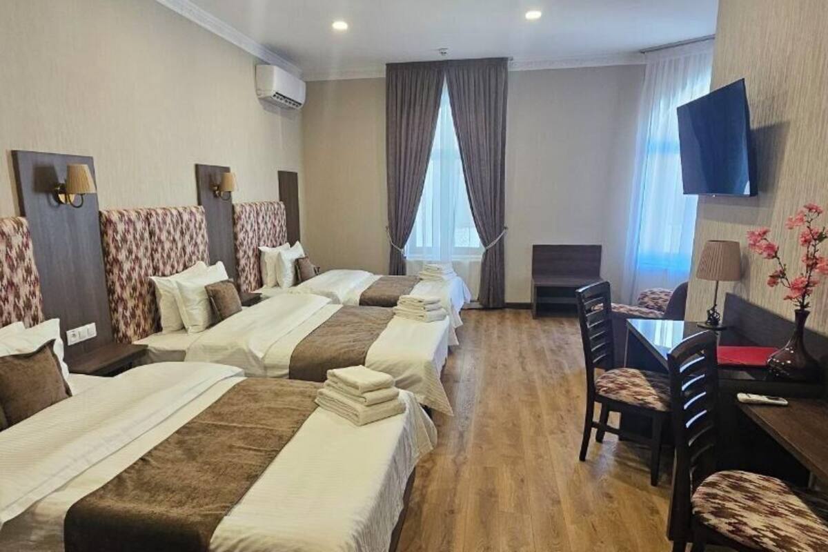 Una habitació d'hotel amb quatre llits, una taula de treball, una cadira, un televisor i una finestra amb cortines.
