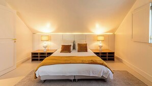 Un dormitorio con cama, mesitas de noche, lámparas y una ventana.