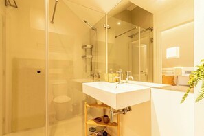 Un baño moderno con ducha envuelta en vidrio, un lavamanos blanco y un espejo.