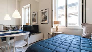 A modern hotel room with a large bed, a dining table, a TV, and a window with a view.