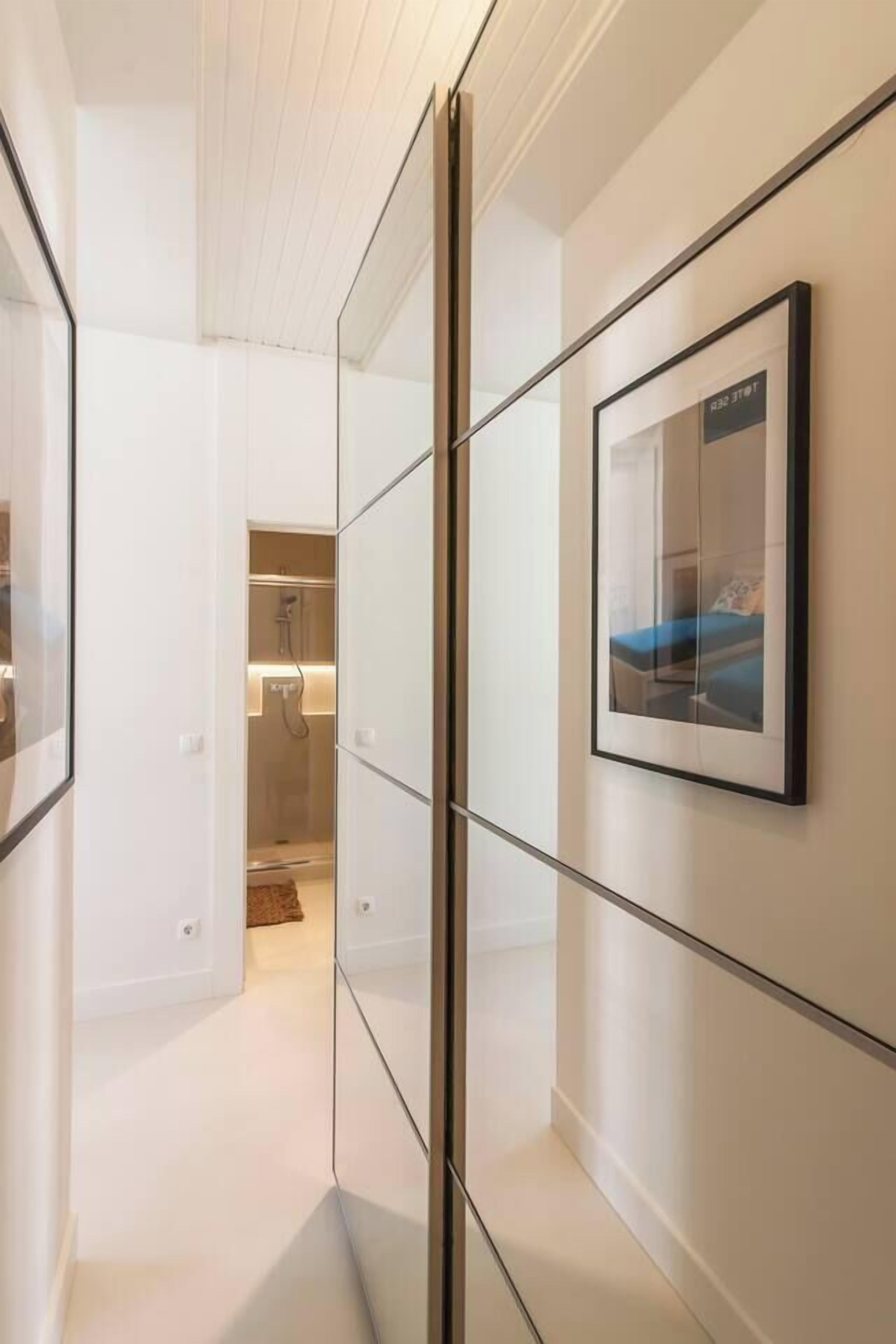 Ein moderner Hotelgang mit Glastrennwänden, einem gerahmten Bild an der Wand und einem Blick auf ein Badezimmer mit Dusche.