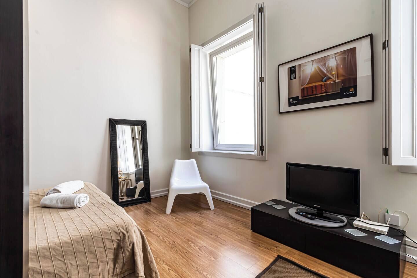 Habitación de hotel con cama, televisión, espejo, ventana y un cuadro en la pared.