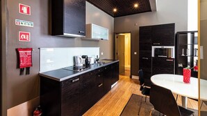 A modern kitchen with dark cabinetry, a built-in microwave, and a coffee machine. There is a dining area with a white table and chairs. - Well-located Studio with Smart Space (Lisbon)