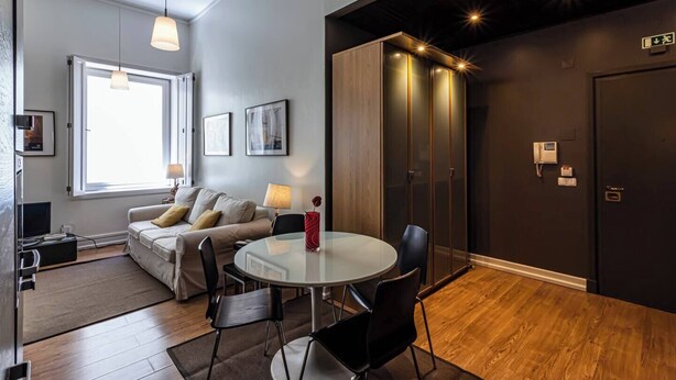 A modern hotel room with a sofa, a round dining table, and a large window. - Well-located Studio with Smart Space (Lisbon)
