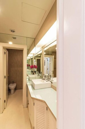 A modern bathroom with a large mirror, two sinks, and a toilet.