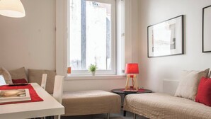 A small, well-lit room with a bed, a desk, and a window.