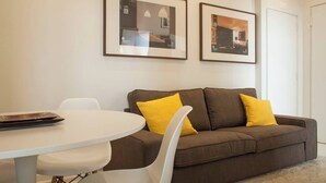 A modern living room with a brown sofa, two yellow cushions, a white table, and two framed pictures on the wall.
