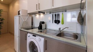 A compact kitchen with a washing machine, a coffee maker, and a sink.