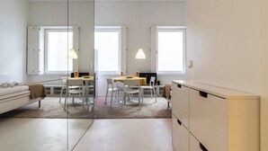 A modern, well-lit room with a bed, a dining table with chairs, and a small kitchen area.