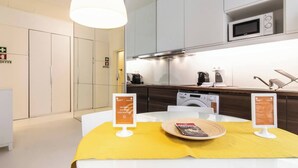 A modern kitchen with a microwave, coffee maker, and dishwasher. There is a yellow table with a magazine and a sign.