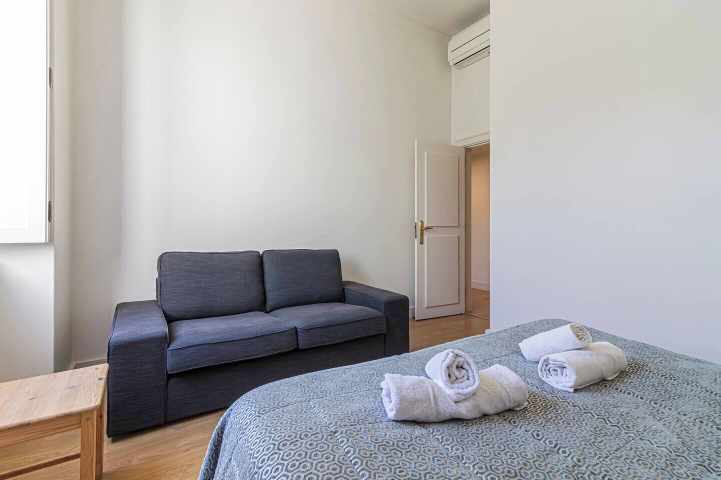 A minimalist room with a grey sofa, a patterned bed, and a wooden bench.
