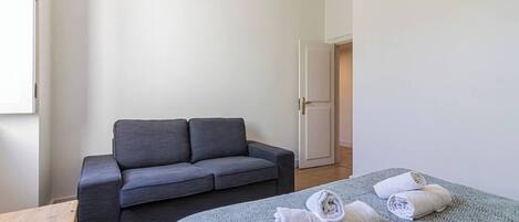 A minimalist room with a grey sofa, a patterned bed, and a wooden bench.