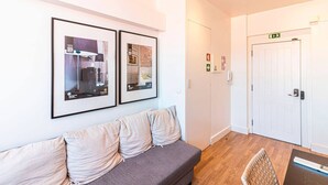 Una hall moderna con un divano grigio, quadri appesi alle pareti, una porta bianca con la segnaletica di uscita di emergenza e un pavimento in legno.