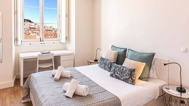 Una camera da letto con un letto, una scrivania e vista su una località costiera attraverso una finestra.
